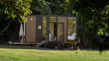Une petite cabane moderne, avec une façade en bois, une porte en verre et un petit espace porche.