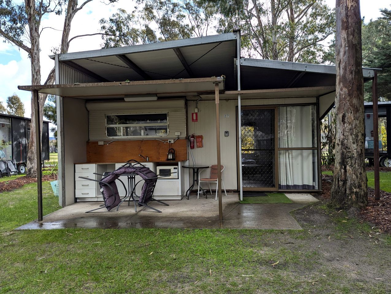 A small, single-story building with a covered outdoor area, a kitchenette, and a dining table with chairs.