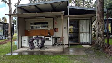 A small, single-story building with a covered outdoor area, a kitchenette, and a dining table with chairs.