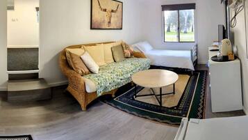 A room with a sofa, a small round table, a bed, a window, and a kitchen area.