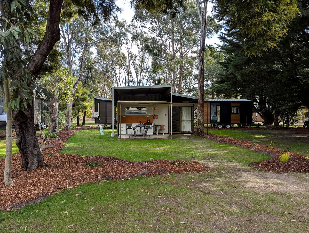 Una casa moderna con una zona esterna coperta, immersa tra alberi e un prato.
