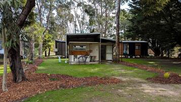 Una casa moderna con una zona esterna coperta, immersa tra alberi e un prato.