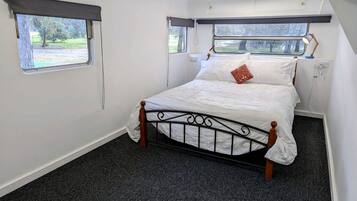 A single bed with a metal frame and wooden headboard in a room with carpeted flooring and two windows with curtains.
