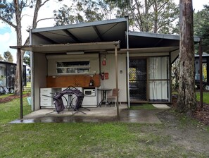 A small, single-story building with a covered outdoor area, a kitchenette, and a dining table with chairs.
