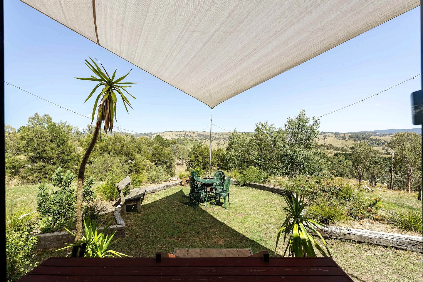 Een terras met een tafel en stoelen, omgeven door groen en uitzicht op een glooiend landschap.