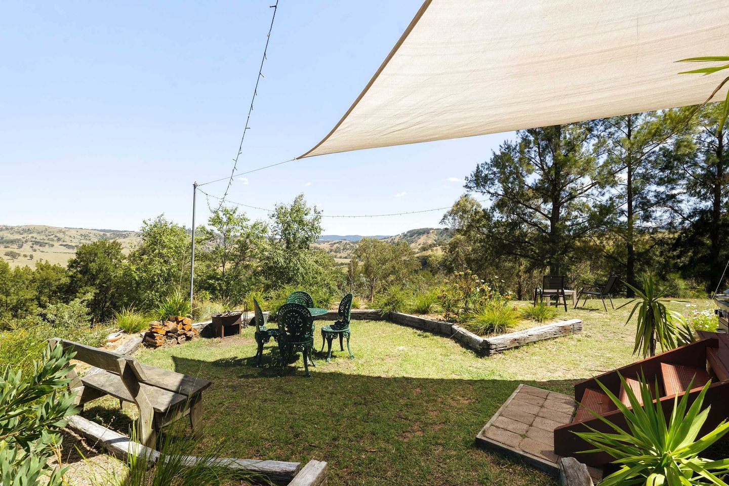 Un jardin avec une table et des chaises en bois, entouré d’une clôture en bois, et un grand arbre en arrière-plan.