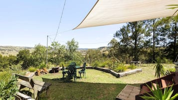 Un jardin avec une table et des chaises en bois, entouré d’une clôture en bois, et un grand arbre en arrière-plan.