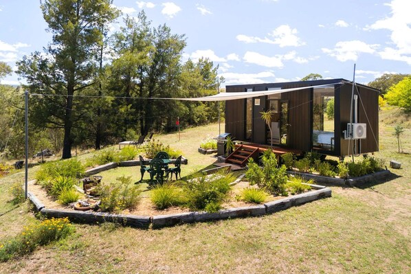 A modern cabin with a deck, surrounded by a landscaped garden with a dining area.