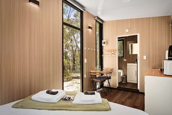 A modern hotel room with a large window, a small dining area, and a kitchenette.