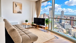 A modern living room with a large window, a sofa, a flat-screen TV, and a city view. - Skyline Rotunda City Apartment I Bullring (Birmingham)