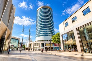 A modern urban plaza with a prominent cylindrical building, a glass-fronted building, and a pedestrian walkway. - Skyline Rotunda City Apartment I Bullring (Birmingham)