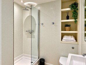A modern bathroom with a glass-enclosed shower, a white sink, and a shelf with towels and a plant. - Skyline Rotunda City Apartment I Bullring (Birmingham)