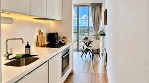 A modern kitchen with a large window, a dining area with a table and chairs, and a view of a cityscape. - Skyline Rotunda City Apartment I Bullring (Birmingham)