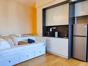 Een compacte slaapkamer met een bed, nachtkastjes en een kitchenette, inclusief een koelkast, magnetron en wastafel.