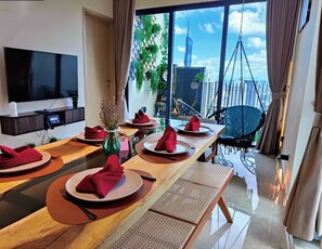 Een moderne eetruimte met een lange tafel gedekt voor meerdere gasten, een flatscreen televisie aan de muur en uitzicht op een stadsbeeld door grote ramen.