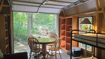 A compact room with a dining table and chairs, a bunk bed, and a window overlooking a forest.