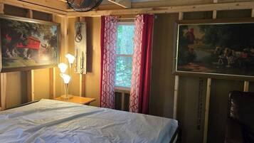 A room with a bed, a desk with a lamp, a window with curtains, and two paintings on the walls.