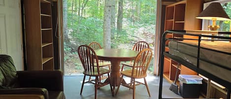 Una habitación acogedora con una mesa de comedor y sillas, una cama litera y vistas a un bosque a través de un ventanal grande.