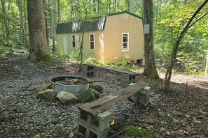 A rustic cabin with a fire pit and benches in a wooded area.