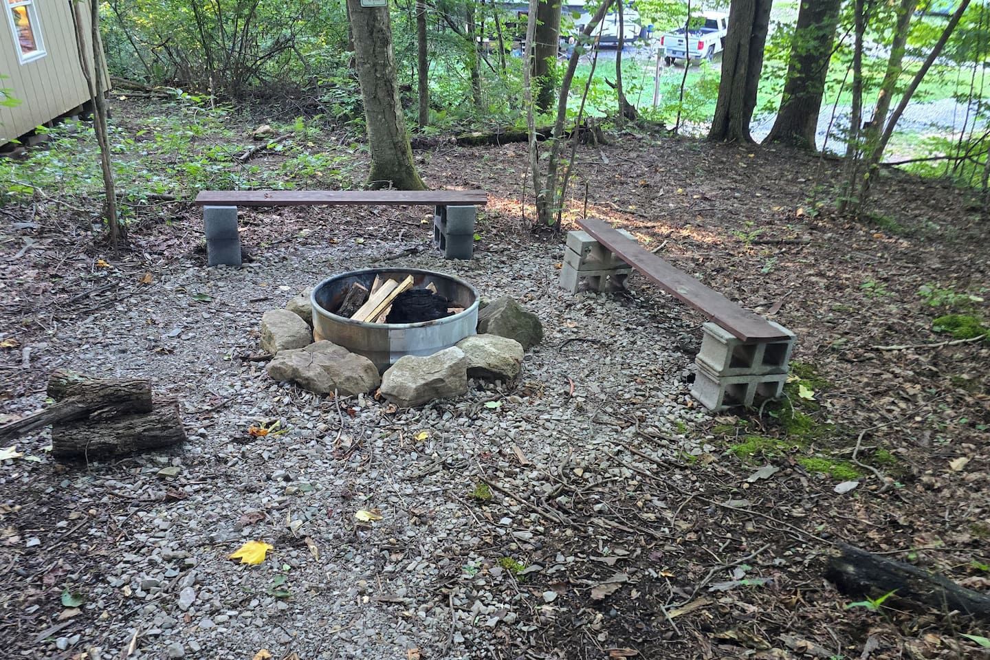 A campsite with a fire pit surrounded by rocks, a bench, and a small structure.