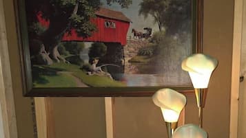 Une pièce comprenant un lit, un tableau représentant un paysage rural et une table sur laquelle sont posées trois lampes.