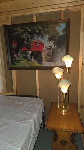 Una habitación con una cama, un cuadro de una escena campestre y una mesa con tres lámparas.