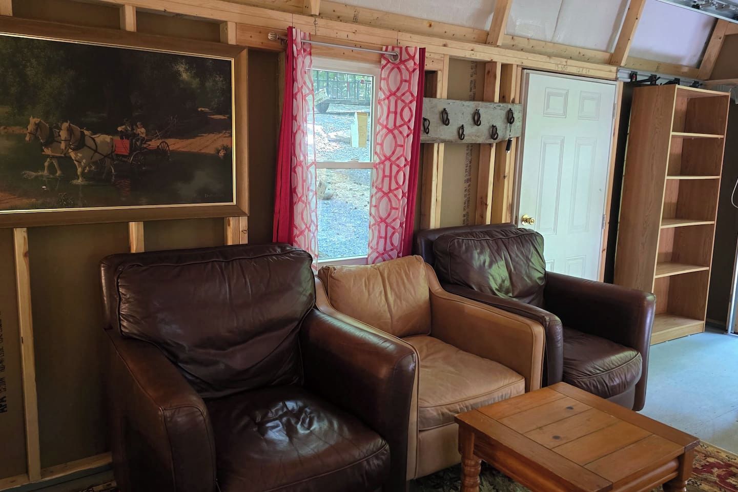 A room with leather sofas, a wooden coffee table, a painting on the wall, and a door leading outside.