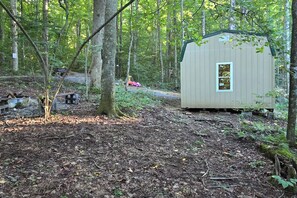A small wooden cabin in a forested area with a dirt path leading to it.