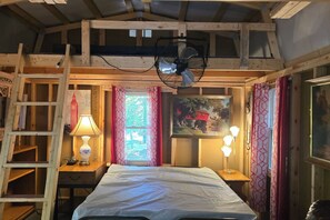 A room with a bed, a fan, a lamp, a ladder, a window with curtains, and a painting on the wall.