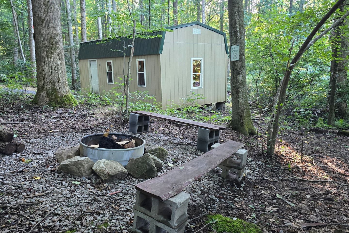 A cabin with a fire pit and a bench in a forest setting.