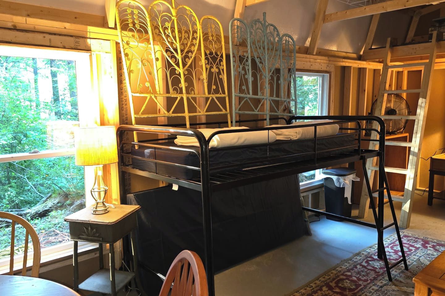 A bunk bed with a metal frame and a window with a view of greenery.