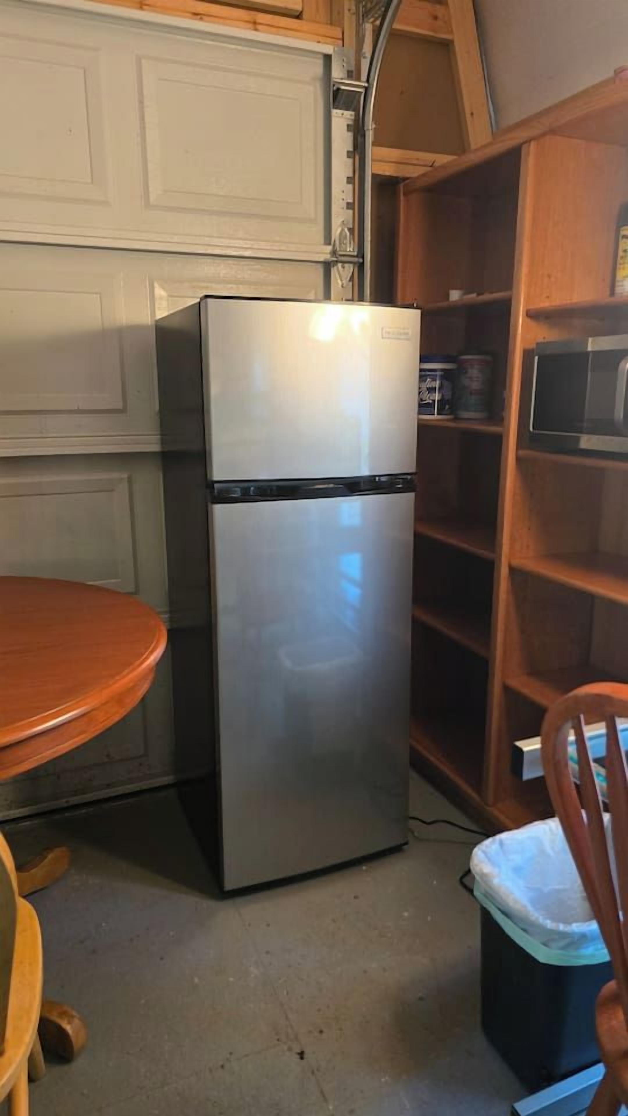 Eine kleine Küche mit einem Edelstahlkühlschrank, einem Holztisch und einem Stuhl.