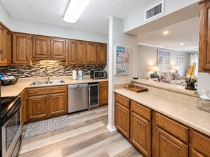 A modern kitchen with wooden cabinets, a dishwasher, and a microwave. - Barefoot Hideaway | Beach + Pool + Boat Friendly + Lagoon | Sea Oats (Gulf Shores)