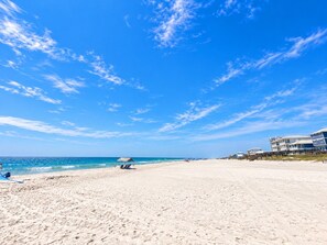 Une plage avec un ciel dégagé, une rive sablonneuse et un immeuble à plusieurs étages situé sur la droite.