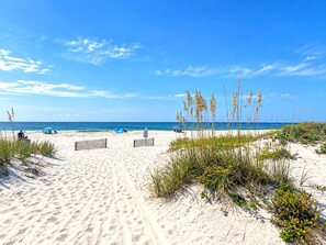 A sandy beach with a clear sky, a few people, and some vegetation. - Barefoot Hideaway | Beach + Pool + Boat Friendly + Lagoon | Sea Oats (Gulf Shores)