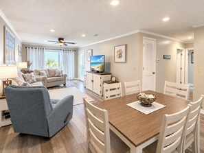 Un salon spacieux comprenant un canapé, une table à manger avec des chaises, un téléviseur et un ventilateur de plafond.