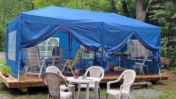 A blue tent with a table and chairs set up on a wooden platform, surrounded by trees.