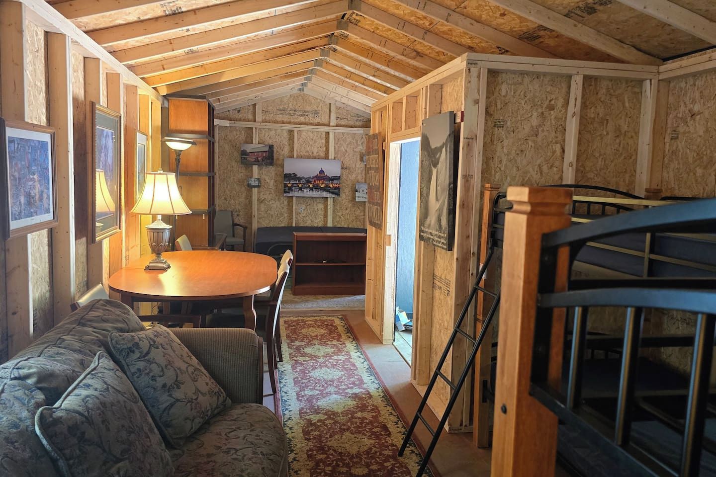 Un'accogliente stanza con soffitto in legno, un tavolo rotondo, un divano e un televisore fissato al muro.