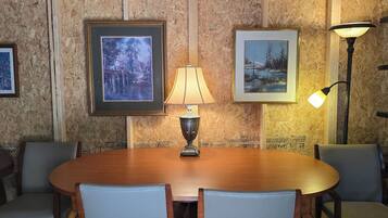 A conference room with a round table, four chairs, two framed paintings, a table lamp, and a floor lamp.