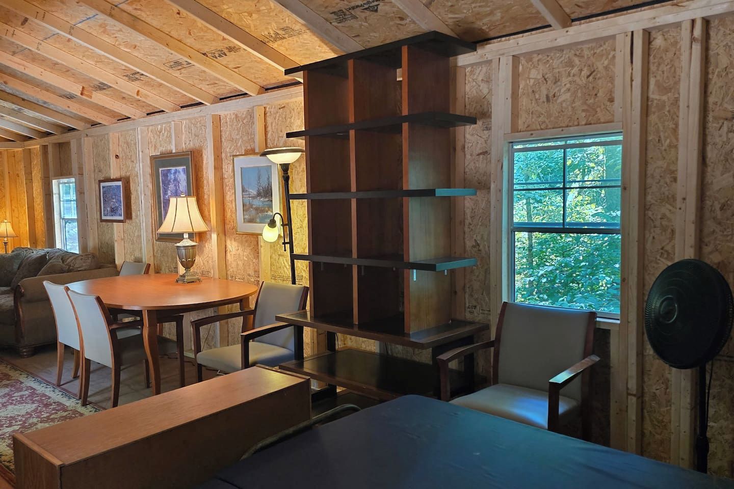 Une pièce avec un plafond en bois, une table à manger avec des chaises, un canapé, une bibliothèque et une fenêtre donnant sur un paysage verdoyant.