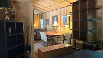 A room with a wooden ceiling, a dining table with chairs, a sofa, and a bookshelf.