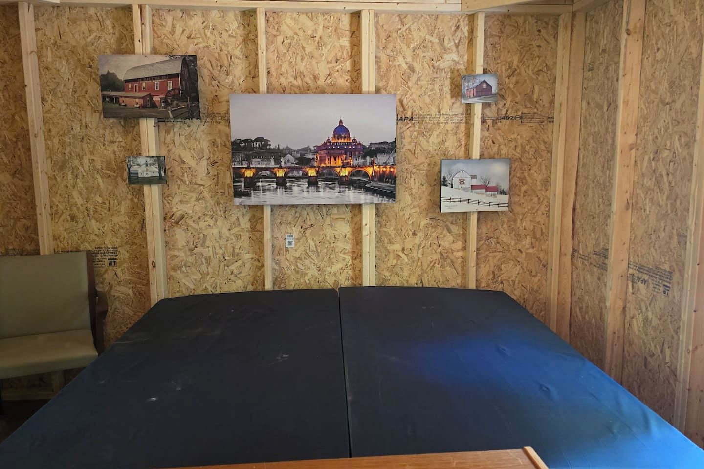 A room with a bed, a chair, and a wall with framed pictures.