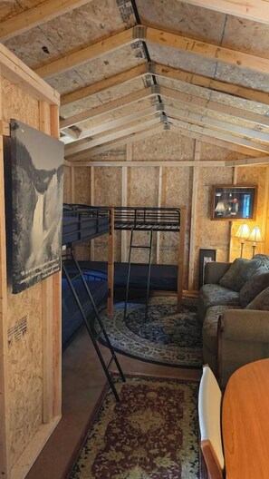 A room with a bunk bed, a couch, a lamp, and a poster on the wall. - D1 Dryfork Forest Retreat-electric-heat (Parsons)