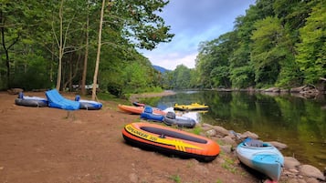 A riverbank with several inflatable rafts and a kayak.