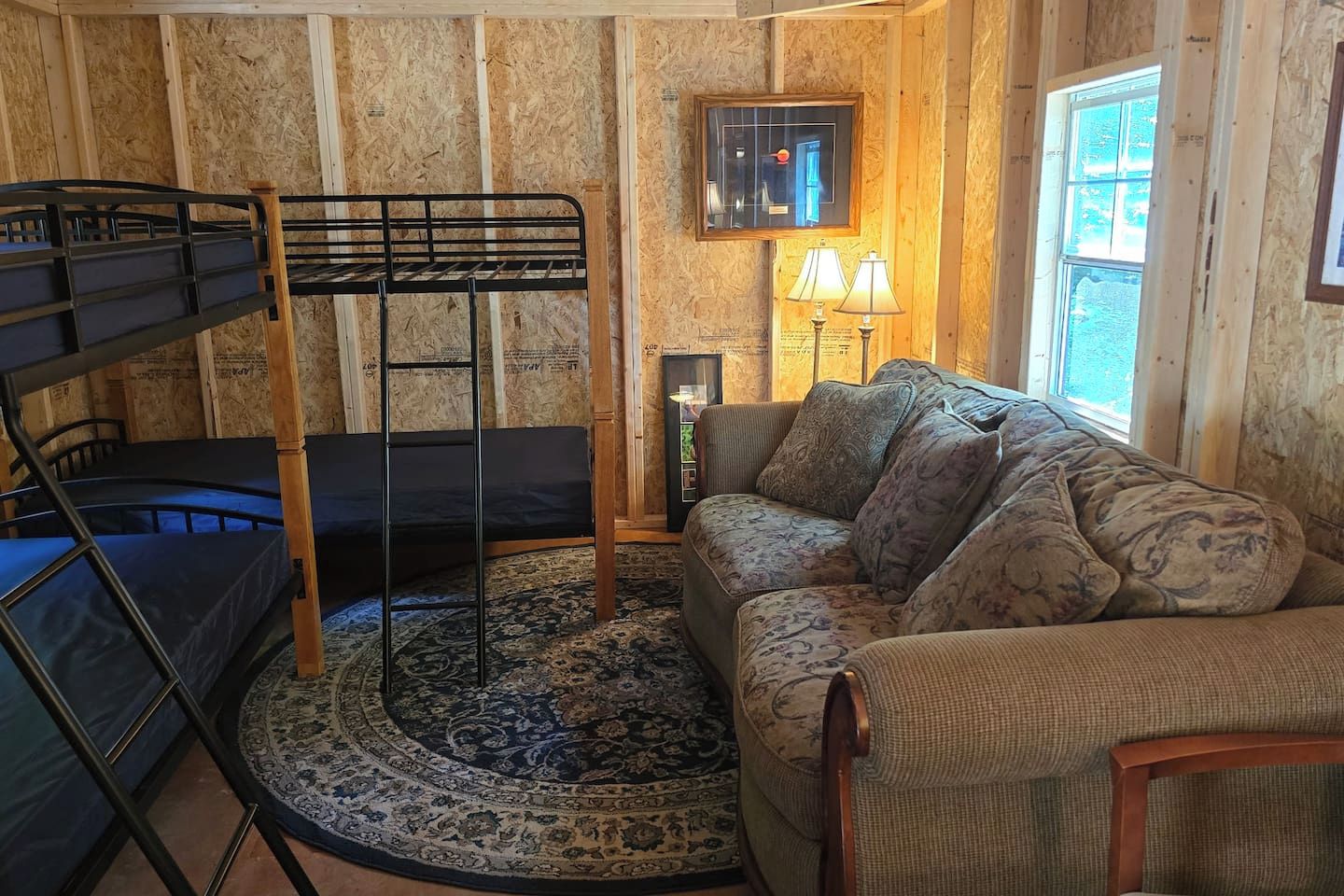 Une pièce avec des lits superposés, un tapis à motifs, un canapé avec des coussins, une lampe et une fenêtre.