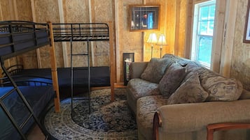 Une pièce avec des lits superposés, un tapis à motifs, un canapé avec des coussins, une lampe et une fenêtre.