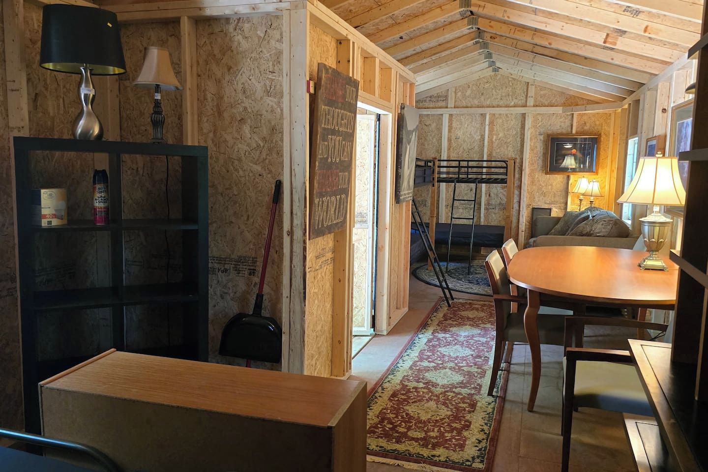 A room with a wooden ceiling, a dining table with chairs, a bookshelf, and a ladder.