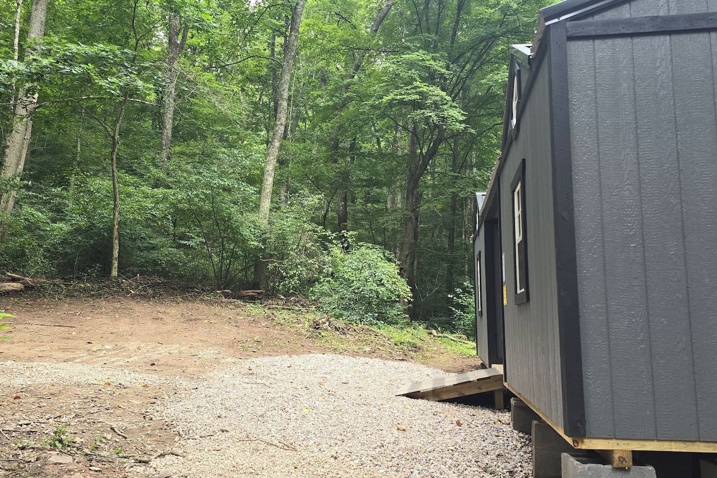 A wooden cabin with a gravel path leading to it, surrounded by dense forest.
