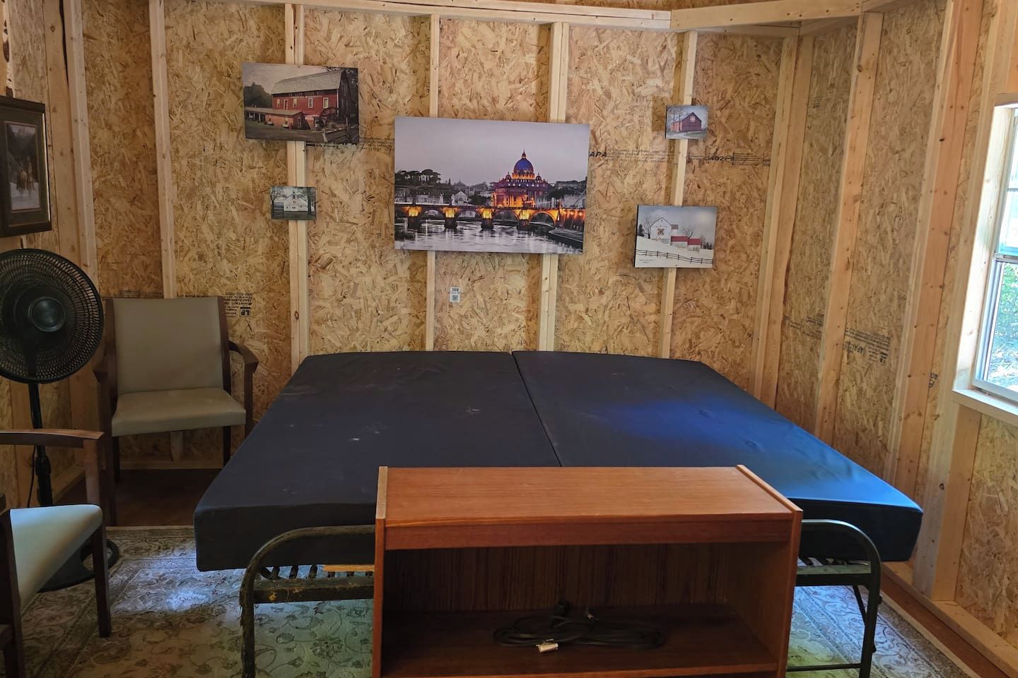A room with a large bed, a chair, a fan, and a window.