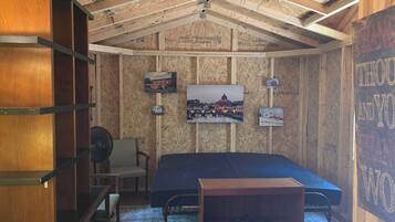 Una stanza con un letto, una sedia, un ventilatore e quadri appesi alle pareti.